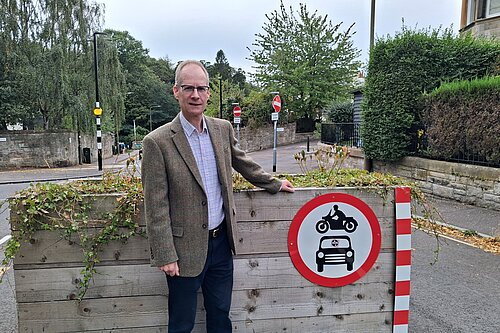 Councillor Neil Ross standing next to a "no cars and no motorbikes" sign on a planter